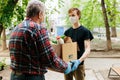 A grocery store delivery man wearing a black polo-shirt delivering food to an old man at home