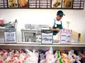 A grocery store workers chops up fresh meat at a meat section of a grocery for a customer.