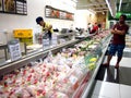 A grocery store workers chops up fresh meat at a meat section of a grocery for a customer.