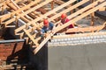 Two workers roofers in helmets surrounded by rafters and beams at construction site build house. Pair of carpenters set