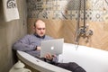 GRODNO, BELARUS - MARCH 2019: young man employees lays in bath with notebook computer in modern luxury plumbing store