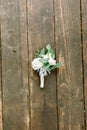 Groom boutonniere from white flowers and greenery on wooden background, rustic decor. Wedding accessory for groom. Royalty Free Stock Photo