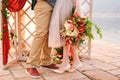 Groom and bride with a bouquet of flowers stand on a stone tile against the background of a carved screen decorated with Royalty Free Stock Photo