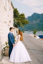 The groom and the bride hold hands and look at each other against the backdrop of a beautiful white house in Perast Royalty Free Stock Photo