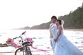 Groom and bride standing on sea beach beside old classic bicycle