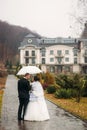 Groom and bride walking in the park on their wedding day. Autumn weather. Rair. Couple umbrella Royalty Free Stock Photo