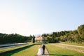 Groom and bride in a white dress with a bouquet of flowers are walking along the path in a beautiful garden against the Royalty Free Stock Photo