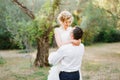 The groom circles the bride in his arms among the trees in the olive grove, the bride smiles