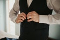 Groom clasping the button of his waistcoat and getting prepared for his wedding