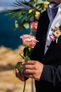 Groom in dark blue suit holding pink rose closeup