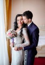 Groom in dark blue suit hugs pretty bride with black curls