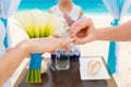 Groom giving an engagement ring to his bride under the arch decorated with flowers on the sandy beach. Wedding ceremony on