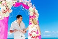 Groom giving an engagement ring to his bride under the arch decorated with flowers on the sandy beach. Wedding ceremony on Royalty Free Stock Photo