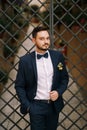 Groom in a gray suit with a bow tie stands near the metal decorative gate Royalty Free Stock Photo