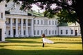 The groom holds the bride in his arms, against the background of a white historical building Royalty Free Stock Photo