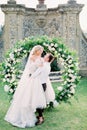 Groom holds bride in his arms at the wedding arch in the garden