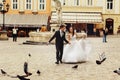 Groom holds bride`s hand while they run across a city square ti Royalty Free Stock Photo