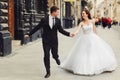 Groom holds bride`s hand tightly while they run along old buildi