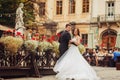 Groom holds bride`s waist posing behind a wooden street cafe