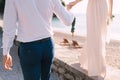 Groom holds the hand of bride with a bouquet, walking along the seashore Royalty Free Stock Photo