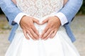 Groom holds his hands in the shape of a heart on the back of the bride in a white dress