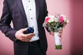 Groom holds wedding bouquet and velvet gift box