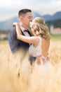 Groom hugging bride tenderly and kisses her on forehead in wheat field somewhere in Slovenian countryside. Royalty Free Stock Photo