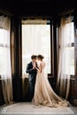 Groom hugs bride against the background of large windows of an old villa. Lake Como