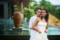 Groom hugs the bride against the beautiful interior with a swimming pool in summer