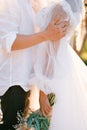 Groom hugs bride with a bouquet by the forearms. Cropped. Faceless. Side view