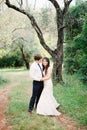 Groom hugs bride near a tree in a green park Royalty Free Stock Photo
