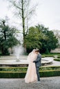 Groom hugs bride in a veil from behind and kisses her on the shoulder, in the garden in front of fountain. Lake Como Royalty Free Stock Photo