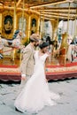 Groom hugs bride in a white dress near the carousel Royalty Free Stock Photo