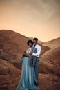 Groom hugs his bride dressed in his jacket in canyon at sunset.