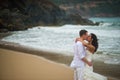 The groom kisses the bride against the sea rocks. couple in love on a deserted beach