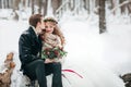 Groom is kissing his bride on the temple on background of the snowy forest. Winter wedding. Artwork