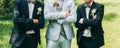 Groom in light blue suit is standing with best man friends. Elegant photo. Outdoors wedding walk. Sunny day.