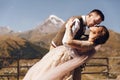 Groom in modern suit and bride in charming pink dress pose on the terasse with great mountain view in Georgia Royalty Free Stock Photo