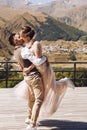 Groom in modern suit and bride in charming pink dress pose on the terasse with great mountain view in Georgia Royalty Free Stock Photo