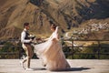 Groom in modern suit and bride in charming pink dress pose on the terasse with great mountain view in Georgia Royalty Free Stock Photo