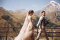 Groom in modern suit and bride in charming pink dress pose on the terasse with great mountain view in Georgia Royalty Free Stock Photo