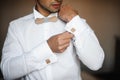 Groom morning preparation. Young bearded groom getting dressed in wedding shirt with wooden bow tie