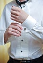 A groom putting on cuff-links as he gets dressed