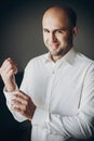 Groom putting on white shirt, standing near window. Stylish man getting ready in the morning in room, preparing for wedding Royalty Free Stock Photo