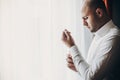 Groom putting on white shirt, standing near window. Stylish man getting ready in the morning in room, preparing for wedding Royalty Free Stock Photo