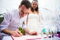 Groom signs documents on registration of marriage and smiles. A young couple signs the wedding documents. Outdoor wedding cere