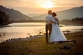 Groom is softly kissing his gorgeous bride in the forehead during the sunset. Wedding picnic on the river bank