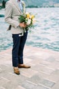 Groom stands on the pier with a bouquet of flowers. Cropped. Faceless