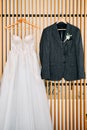 Groom suit and bride dress hang on hangers on a wooden plank wall in a hotel room Royalty Free Stock Photo