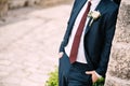 The groom in the suit with a red tie and a boutonniere with white rose on the street of the old town, close-up